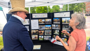 man in a top hat talking to a woman in a pink shirt in front of a display